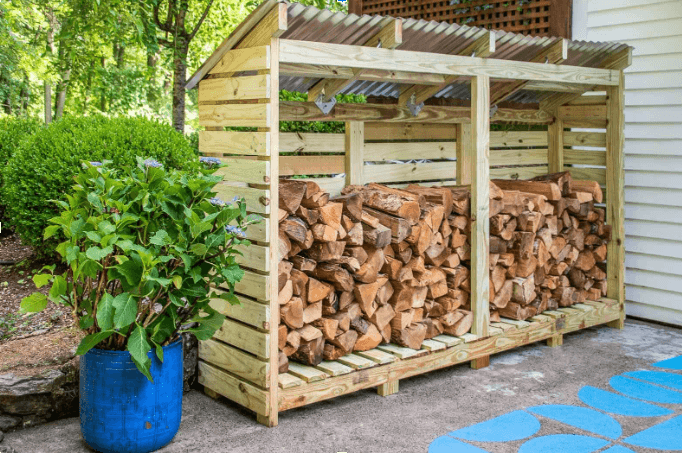 A wooden firewood shed with a corrugated metal roof